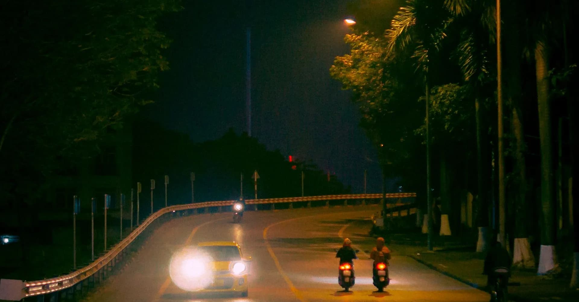 Motorcycles and a car travelling along a city road at night